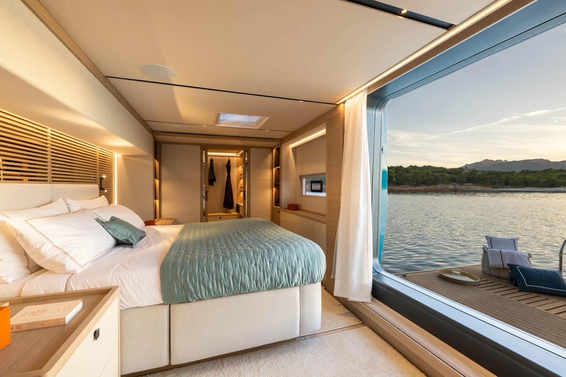Owner's suite of the Lagoon Eigthy2 with a wide bed and a panoramic window over the water at sunset